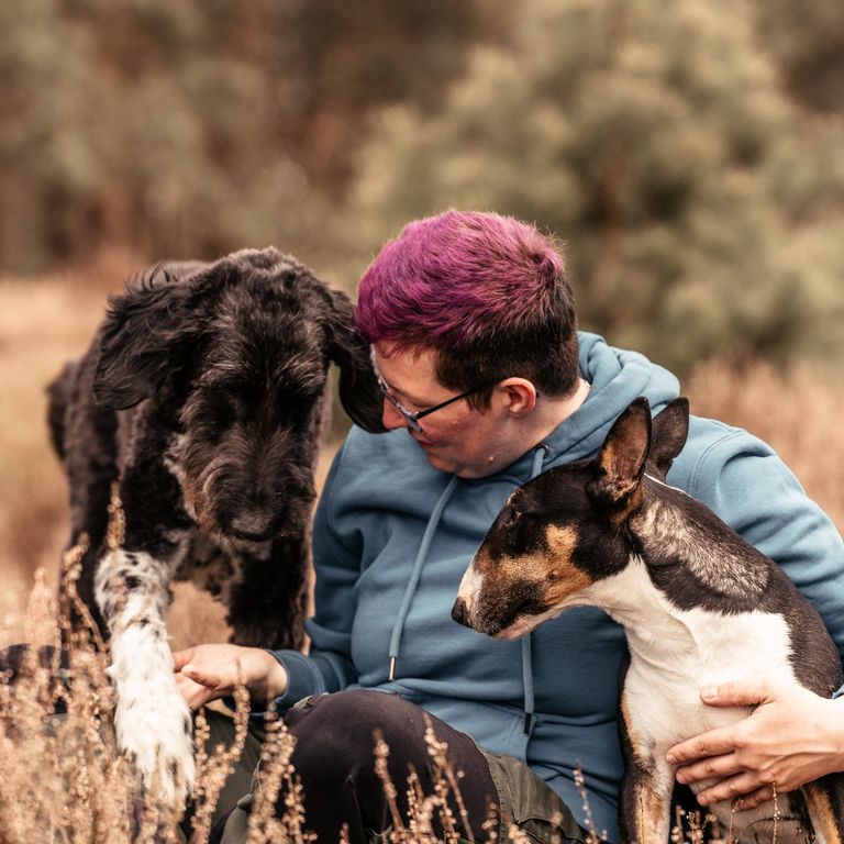 Eine Frau sitzt mit zwei Hunden in der Lüneburger Heide. Der Hund gibt der Frau die Pfote