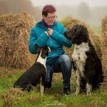 Eine Frau sitzt mit zwei Hunden vor einem Strohballen.